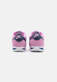 Nike sneakers featuring a pink suede upper, navy accents, padded collar, and white sole with blue detailing, showcased from the back.