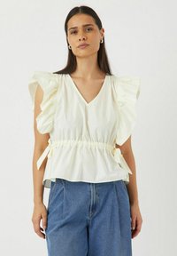 Lichtgele blouse met een V-hals, volumineuze ruches mouwen, gathered taille met strikjes en een zachte, gladde textuur. Gecombineerd met blauwe denim broek.