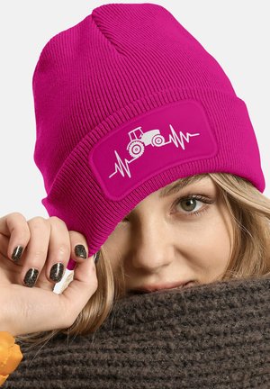 Bright pink knitted beanie with ribbed texture, featuring a white tractor design and heartbeat line on a rectangular patch.