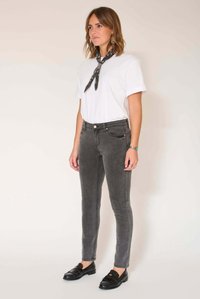 Jean skinny gris avec poches avant, associé à un t-shirt blanc et une écharpe noire à motifs. Des chaussures plates noires complètent le look.