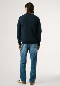 Jūros laivyno tekstūruotas megztinis su apvaliu kaklu, derinamas su šviesiai mėlynais laisvais cargo džinsais, turinčiais šonines kišenes ir kontrastingą siūlę.