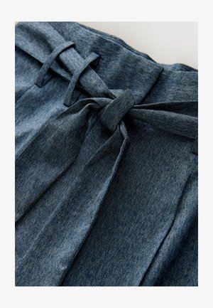 Dunkler Denimstoff mit Fischgrätenmuster, versehen mit einem gebundenen Taillendetail und überlappenden Stofffalten für Textur.