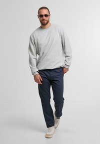 Grauer Pulli mit langen Ärmeln, kombiniert mit navyblauen Hosen. Weiße Sneakers mit strukturierten Akzenten. Modell geht vor einem hellen Hintergrund.