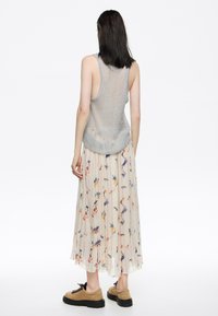 Top de punto gris claro sin mangas con la espalda abierta, combinado con una falda larga y fluida de color crema con estampado floral, que presenta pliegues y una textura ligera.