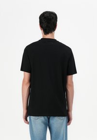 Black cotton t-shirt with a classic crew neck and short sleeves. Features minimalistic design with subtle branding on the back.