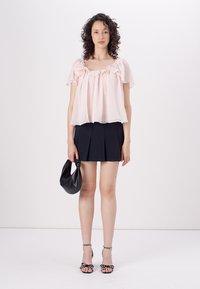 Top rosa trasparente con scollatura arricciata, abbinato a una mini gonna a pieghe nera. Borsa nera e sandali con tacchi e borchie.