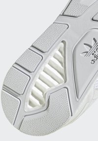 Balta sporta apavu zole, kas izgatavota no teksturēta gumijas ar izteiksmīgām paceltām rakstām, rievām stabilitātei un Adidas logotipa detaļu.