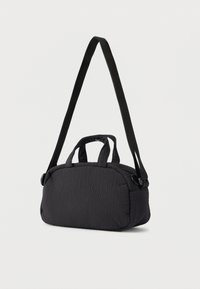 Petit sac à main noir texturé avec des poignées courtes et une longue bandoulière réglable sur un fond uni.