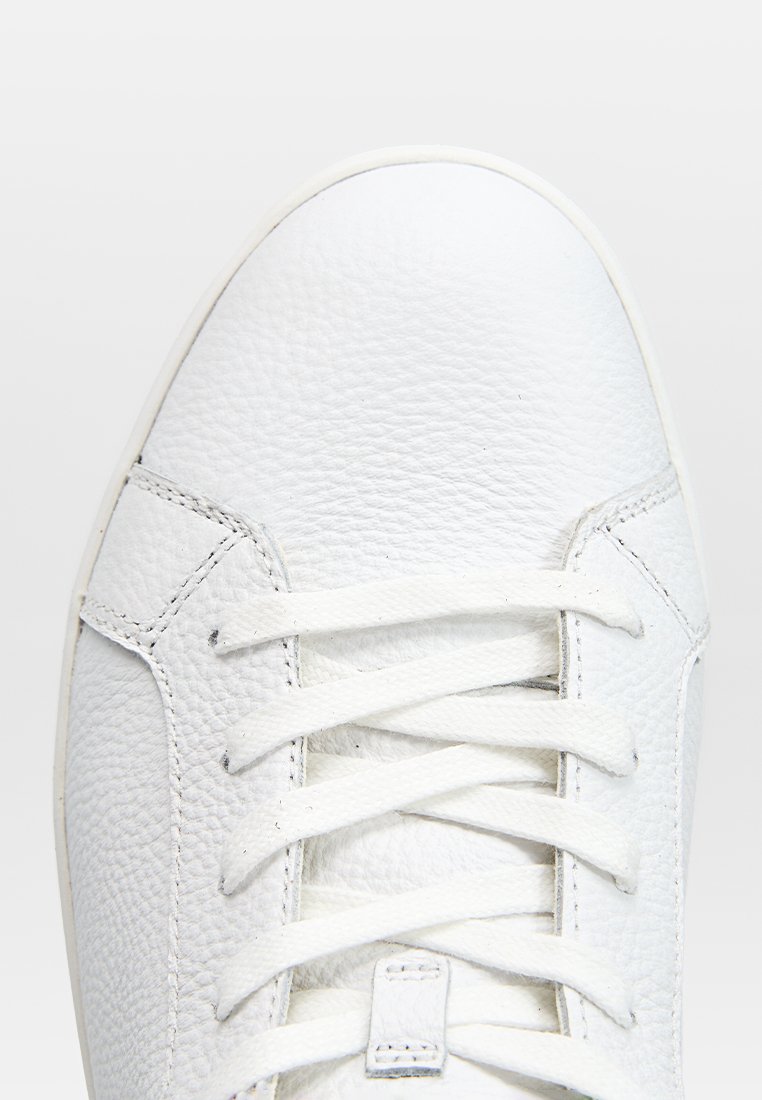 Białe skórzane trampki z teksturowaną cholewką, klasycznym wiązaniem oraz smukłą sylwetką z minimalną ilością przeszyć.