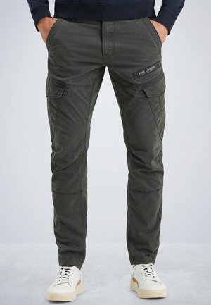 Pantalon cargo vert foncé avec plusieurs poches, porté par une personne debout les mains dans les poches, assorti à des baskets blanches.