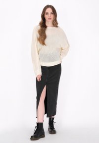 Dikke crème gebreide trui met brede mouwen, in combinatie met een zwarte denim rok met een hoge split. Zwarte veterschoenen maken de look compleet.