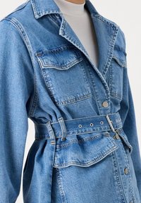 Giubbotto di denim in blu chiaro con vita regolabile, dotato di due tasche sul petto e chiusure a bottone, colletto strutturato e vestibilità rilassata.