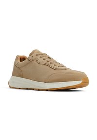 Zapatilla deportiva de ante beige con puntera redondeada, lengüeta elevada y entresuela blanca. Presenta una suela de goma texturizada con patrón antideslizante.