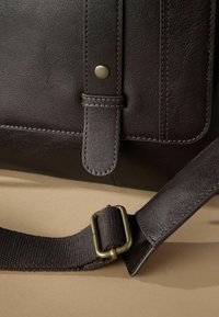 Dark brown leather messenger bag with a smooth texture, featuring a front flap, brass hardware, and an adjustable fabric strap.