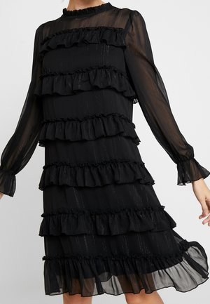 Zwarte doorzichtige jurk met lange mouwen, meerdere horizontale ruches en subtiele verticale glinsterende lijnen, lengte tot halverwege de dij.