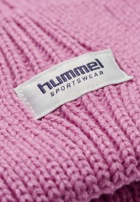 Roze gebreide stof met een geribbelde structuur, met een wit label waarop de tekst "hummel SPORTSWEAR" in donkerblauw staat.