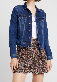 Mörkblå denimjacka med knäppningar, två bröstfickor och en kortad design. Matchad med en svart blommig volangkjol.