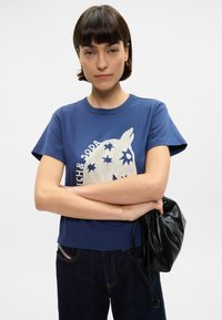 Μπλε βαμβακερό T-shirt με στρογγυλή λαιμόκοψη, κοντά μανίκια και γραφική εκτύπωση ενός αλόγου και άστρων σε λευκό χρώμα. Συνδυάζεται με σκούρο τζην.