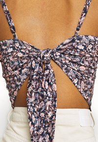 Blommig crop top med marinblå bakgrund, prydd med rosa och vita mönster, knuten bak, och tunna justerbara axelremmar.