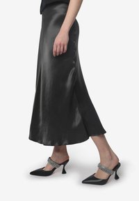 Zwarte satijnen midi-rok met een uitlopende zoom. Gecombineerd met zwarte puntige hakken met een juweelbandje. Glad textuur en elegant ontwerp.