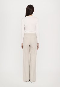 Lichte, aansluitende witte blouse met lange mouwen, gecombineerd met hoogwandaardige, wijdvallende beige broeken, voorzien van achterzakken en een gladde textuur.