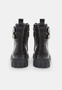 Stivali alla caviglia neri in stampa coccodrillo con suola spessa, caratterizzati da doppie cinghie e finiture metalliche, texture strutturata e linguette per il settore.