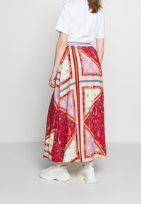 Falda maxi con una vibrante tela roja y patrones intrincados en rosa, blanco y verde. Cintura elástica con detalle a rayas.