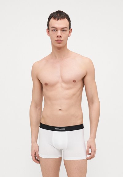 Boxer-briefs blancs avec une ceinture noire portant le texte "DSQUARED2." Le tissu semble lisse et extensible, avec un design moulant.