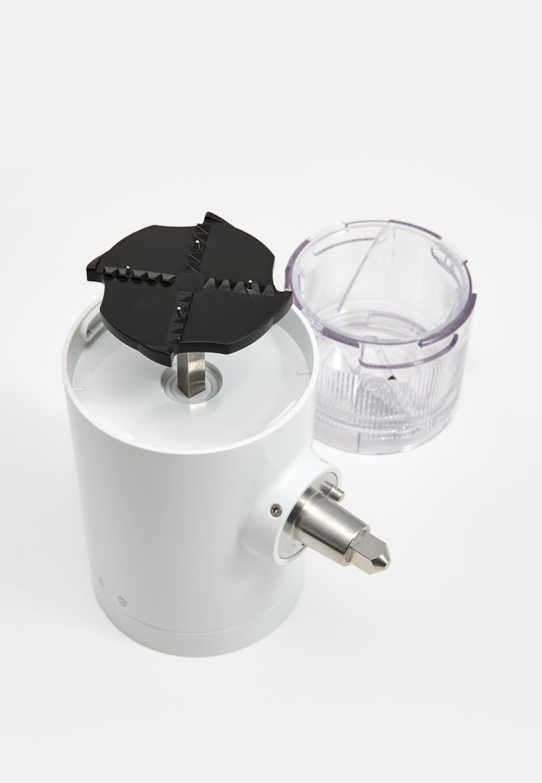 Witte keukenapparaat met een zwart, getand mes aan de bovenkant. Heldere container ernaast met groeven, ontworpen voor voedselverwerking of malen.