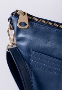 Navy leather handbag with a gold zipper and hardware, featuring a front pocket with horizontal stitching and an adjustable strap.