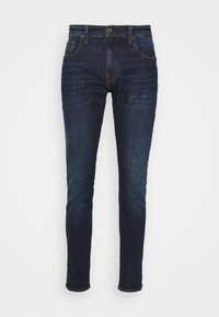 Mörkblå denimjeans i slim fit. Har fem fickor, kontrasterande sömmar och knappstängning. Slät textur.