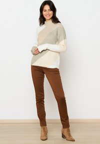 Maglione leggero in beige, crema e salvia con blocchi di colore diagonali. Abbinato a pantaloni marroni aderenti e stivaletti alla caviglia.