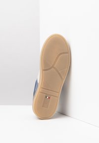 Semelle de sneaker en caoutchouc beige avec un motif texturé, logo "NeroGiardini" et détail du drapeau italien. Tige en tissu bleu et blanc visible.