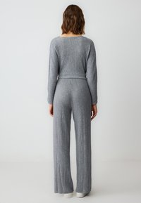 Grijs geribbeld twee-delig outfit met een aansluitend top met lange mouwen en hoge taille, gecombineerd met wijde pijpen en elegante, minimalistische schoenen.