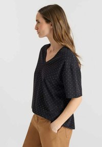 Top negro de manga corta con diseño de escote en V, decorado con lunares blancos. Material suave y ajuste relajado, combinado con pantalones color marrón claro.