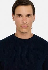 Granatowy sweter z prążkowanego dzianiny, z okrągłym dekoltem i rękawami raglanowymi. Tekstura materiału wydaje się miękka i gruba. Brak widocznych wzorów lub akcentów.