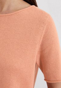Krótki rękaw sweter w miękkim odcieniu brzoskwini, z okrągłym dekoltem i teksturowanym materiałem, luźny krój i subtelne szwy.