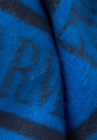 Tissu en laine douce bleu et noir avec une texture duveteuse et des motifs géométriques abstraits, montré en gros plan avec des plis et des ombres.