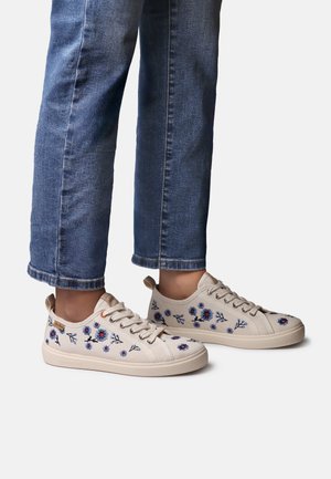 Béžové plátené tenisky s vyšívanými modrými kvetinovými vzormi. Zaoblená špička, viazanie na šnúrky a nenápadná gumová podrážka. Nosené s modrými denimovými džínsami.