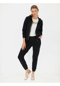 Czarna bluza z zamkiem i sznurkiem, biała koszulka z złotymi literami oraz czarne dresowe spodnie. Uzupełnione lekkimi, wielokolorowymi trampkami.