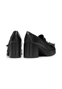 Scarpe platform in pelle nera con punta arrotondata, tacco a blocco spesso e dettagli con nappine decorative sulla tomaia. Superficie del tacco texturizzata.