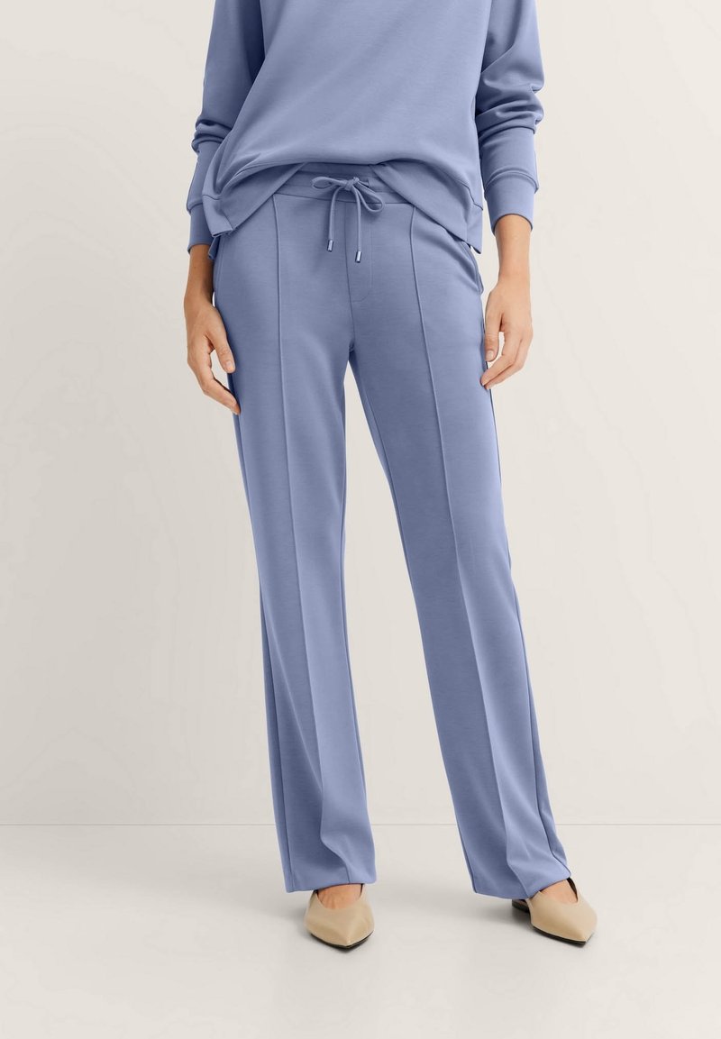 Light blue sweatpants with a relaxed fit, featuring a drawstring waist, side seams, and soft, smooth texture. Paired with beige flats.