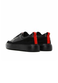 Baskets noires en cuir et velours, avec une semelle en caoutchouc noir texturé et un accent rouge au niveau du talon.