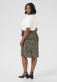 Weißes kurzärmeliges Oberteil kombiniert mit einem knielangen, dunkelgrünen Rock mit Zebra-Print; zusätzliche Details umfassen eine gebundene Taille. Schwarze Schuhe.