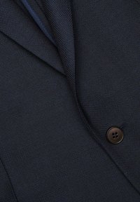 Granatowa marynarka z teksturowanej tkaniny, z klapami i widocznym brązowym guzikiem z przodu. Dopasowany krój o eleganckim wyglądzie.