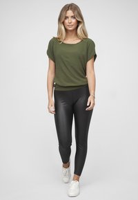 Olivengrønn topp med korte ermer, kombinert med svarte leggings og hvite joggesko. Toppen har en avslappet passform og rund hals.