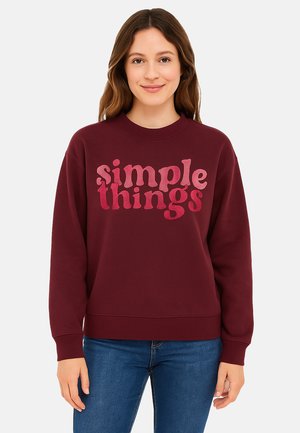 Bordeaux-roter Sweatshirt mit Rundhalsausschnitt, langen Ärmeln und gerippten Bündchen. Mit oversized, pinkem Text "einfache Dinge" in einer verspielten Schriftart.