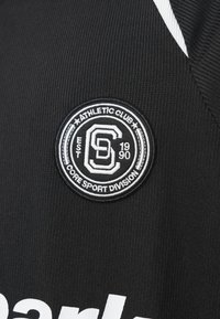 Μαύρο αθλητικό μπλουζάκι με ραβδωτή υφή, με κυκλικό κεντητό λογότυπο σε λευκό και μαύρο, και το κείμενο "Core Sport Division".