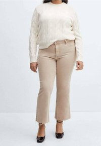 Pull en tricot câblé crème avec un col rond associé à un jean évasé beige clair avec des ourlets effilochés et des chaussures à talons blocs noires.