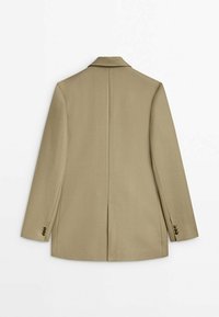 Blazer beige sur mesure avec manches longues, fente au dos et détails de boutons aux poignets, posé à plat montrant le dos.
